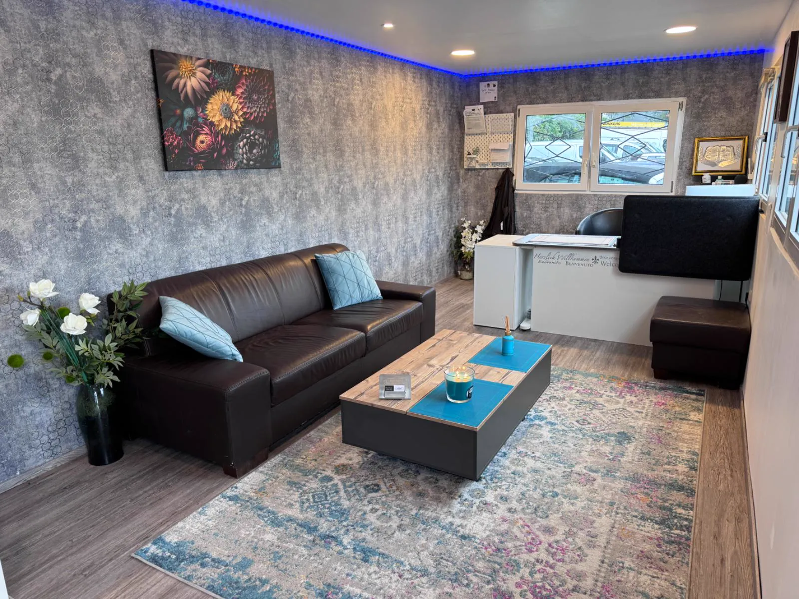 Der Verkaufsraum des Autohof Wentorf: Ledersofa mit türkisen Kissen, Holztisch und Tresen mit „Herzlich Willkommen“