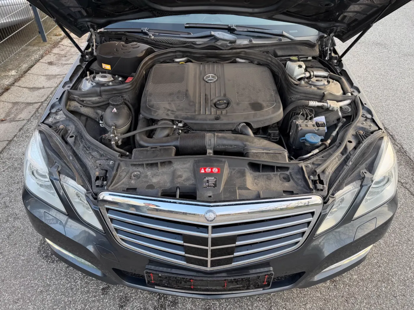 Geöffnete Motorhaube eines grauen Mercedes-Benz E 250 auf dem Hof
